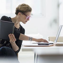 Mujer con gafas con crizal prevencia mirando un ordenador portátil y sosteniendo una tablet